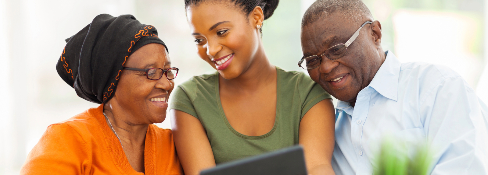 Young woman holding a tablet, showing elderly couple an email newsletter.